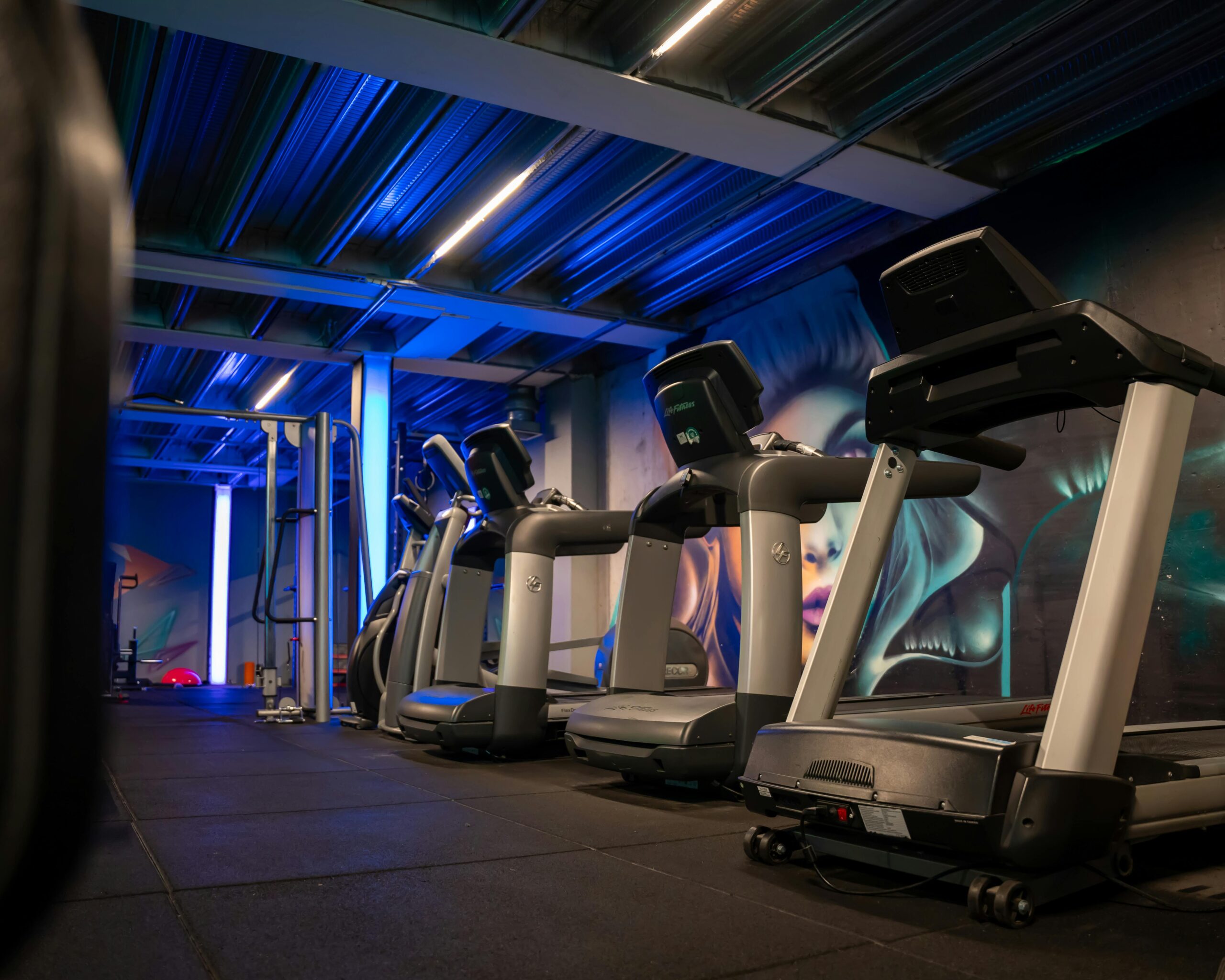 A sleek gym showcasing multiple treadmills with modern blue neon lighting and wall art.